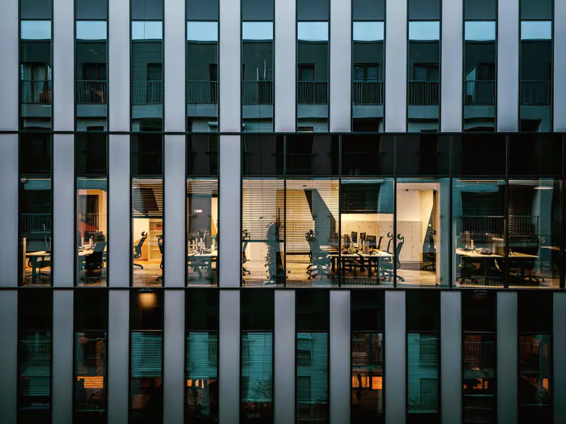 Glass and steel facade of an office building at dusk, its floors lit from inside