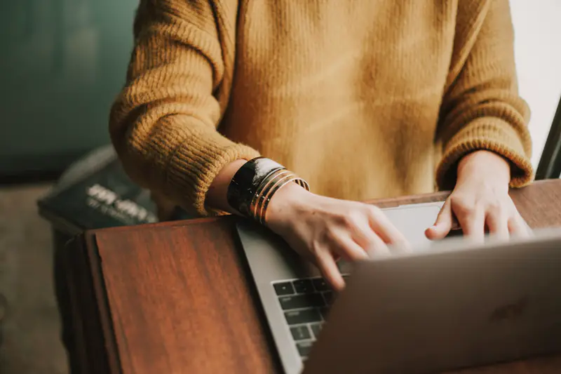 Hands typing on a laptop resting on a wooden desk