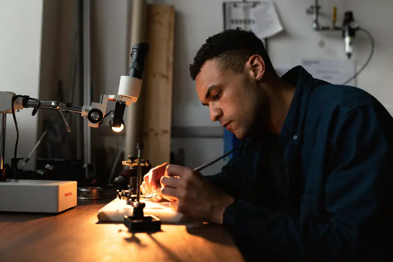 An engineer assembling electronics under a lamp at a workbench