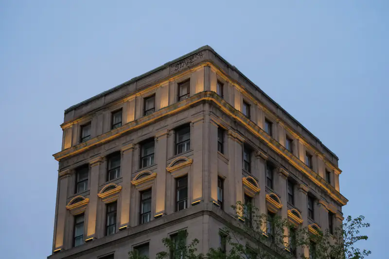 A stone office building with lit cornices against an evening sky
