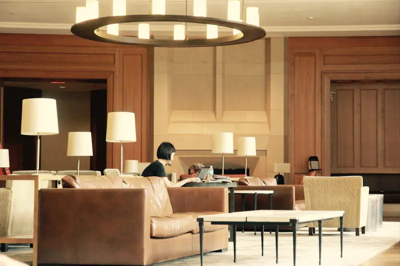 A warmly lit hotel lounge with leather sofas and a guest working at a table