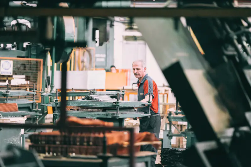 A worker tending machinery on a factory floor, seen through the frame of another machine